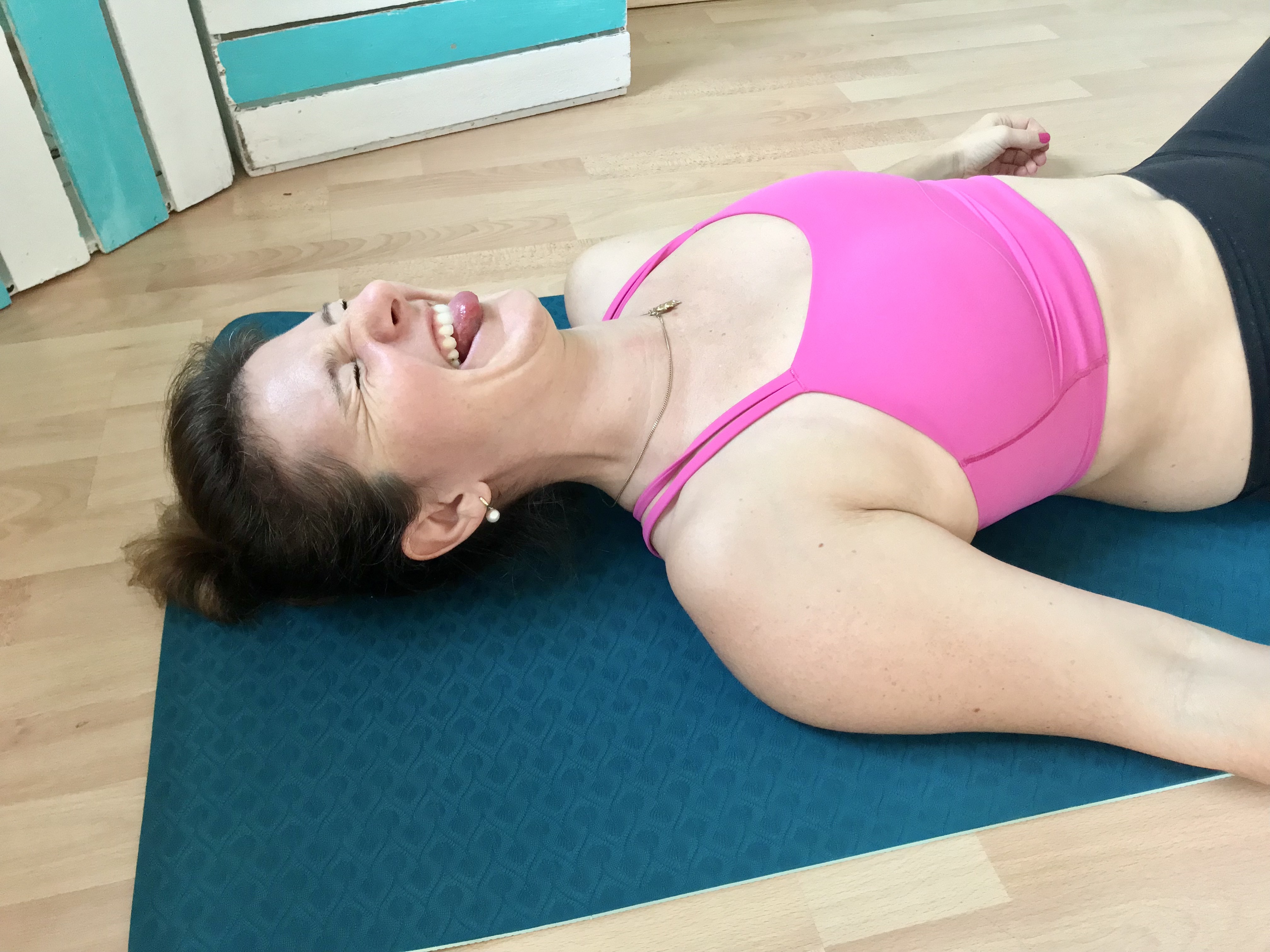 Lachende Frau während der Rückbildung auf einer dunkelgrünen Sportmatte in einem Studio bei Bad Segeberg.